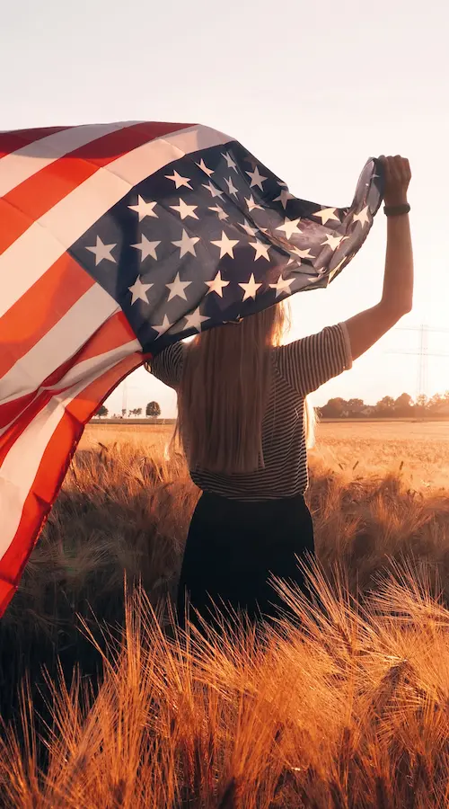 Woman holding American flag in wheat field.