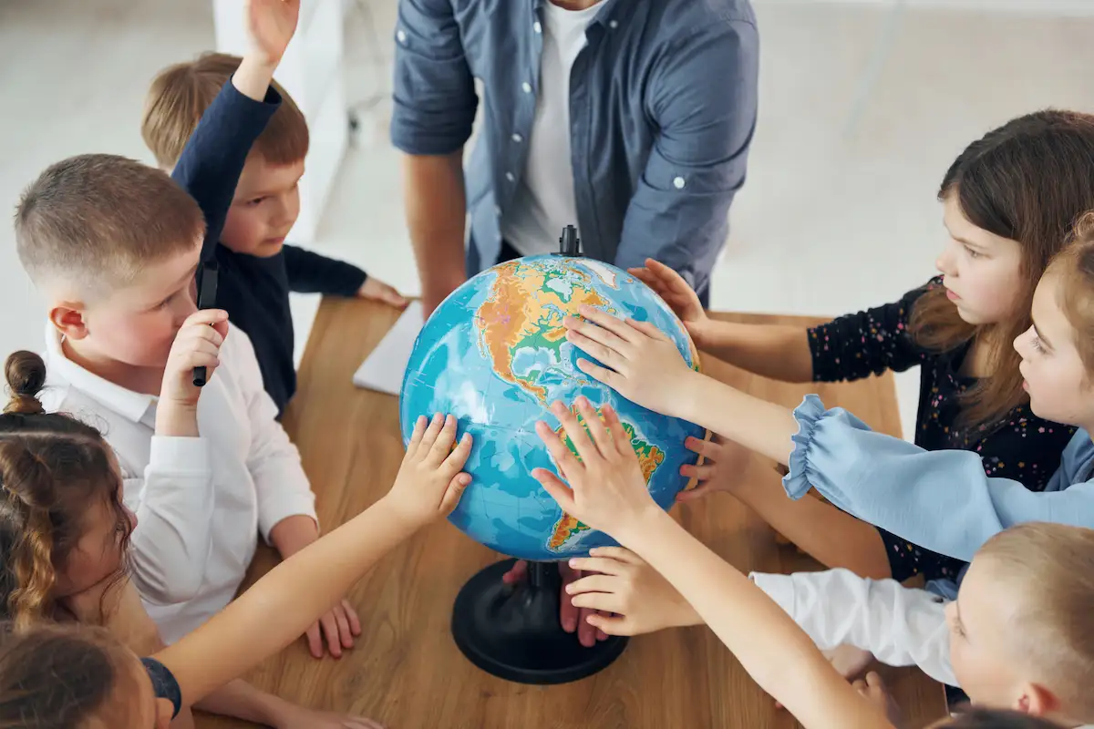 Kids putting their hands on a globe and teacher leaning on table