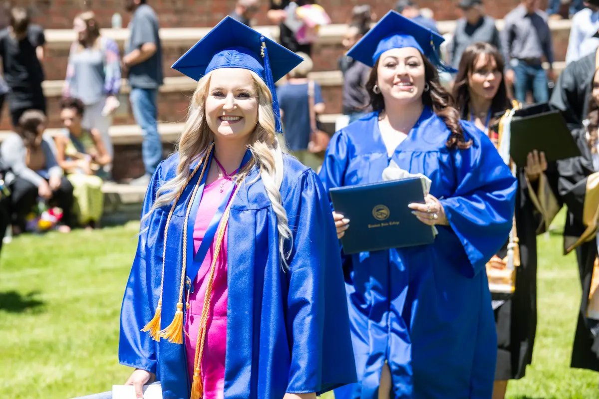 Students smiling in caps and gowns, walking at graduation.