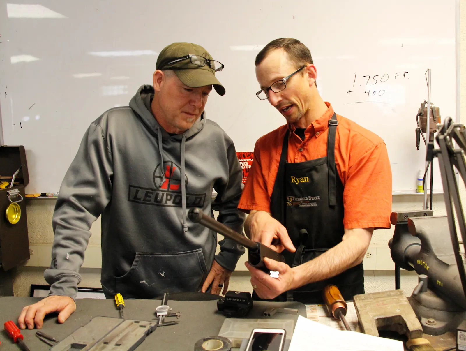 Gunsmithing instructor holding gun part and talking to student.