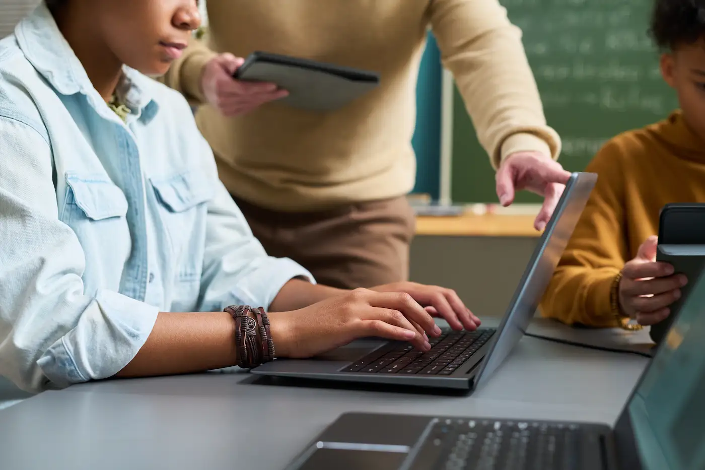 Teacher standing behind student who is working on a laptop